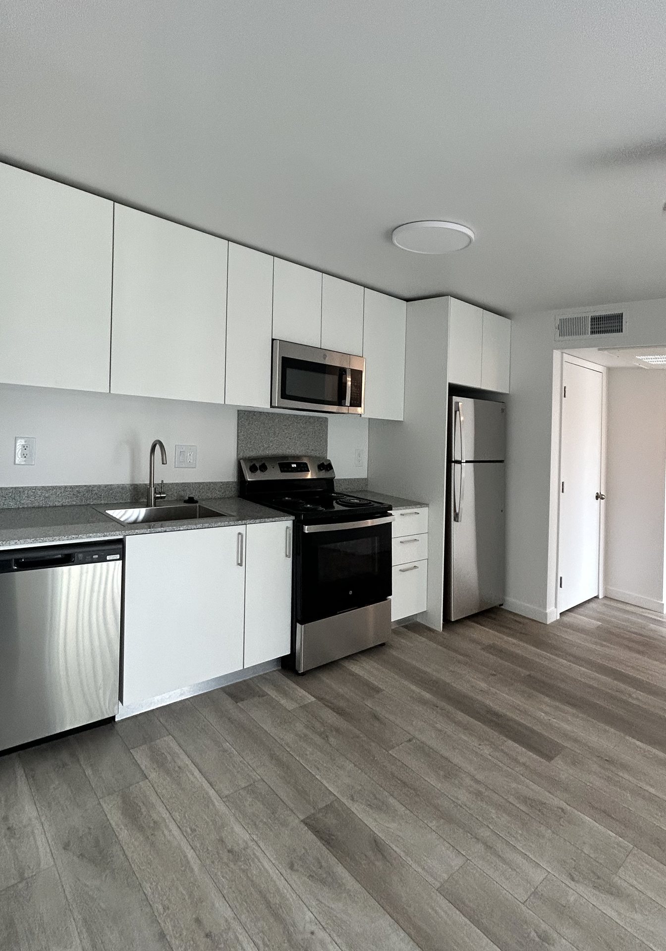 Renovated apartment kitchen at Broadway Restoration with white flat-panel cabinets, granite countertops, stainless steel appliances, and wood-look plank flooring